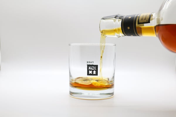 Photo shows the candle container being used as a glass. In the photo, a person is pouring whisky into the glass. This photo is part of the article on How to make candles at home to sell online.