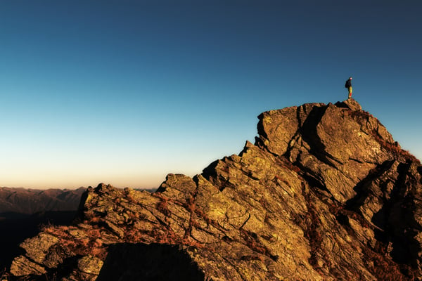 A man on the top of a mountain with a dark blue sky, representing the journey to finding your own purpose.