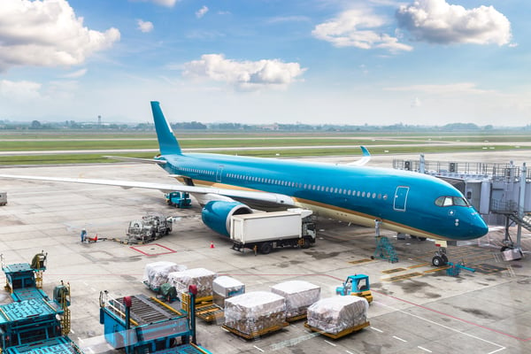 A cargo blue airplane in the airport, with trucks and machines around, representing an exporting country exporting products to a foreign market.