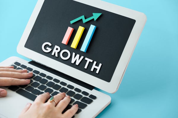 Two hands above a silver laptop with a black keyboard and a black screen with the word "growth" being displayed below a columns chart, as paid traffic is a way to increase results.