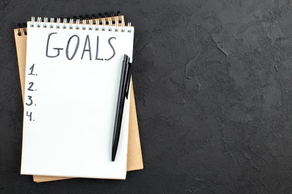 A notebook over a black background with the title "Goals" written on a Task List.