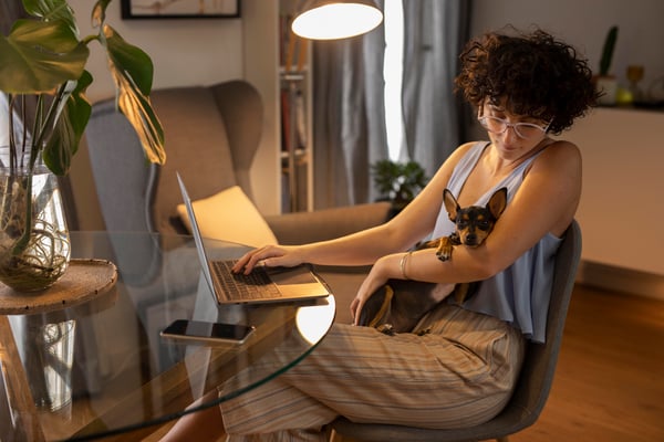 A woman using her laptop at home while holding her dog in her arms, representing how we can make money at home