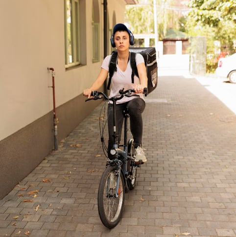 Photo from the green marketing article shows a person on a bicycle, carrying a cooler backpack and wearing headphones and a hat. The person is riding their bike on a quiet street.