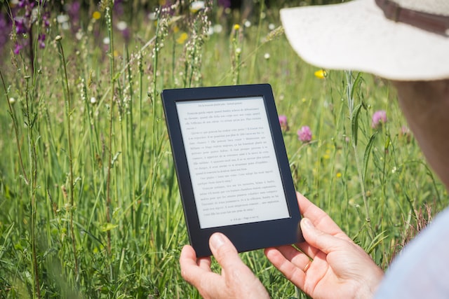 The photo shows a person holding an e-reader in a flower field. The photo was taken from behind the person and focuses on the their hands and e-reader. This photo illustrates the blog post section on starting an online business in Canada by writing ebooks.