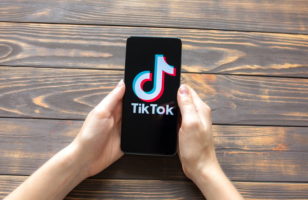 Two hands holding a celphone with the screen displaying the TikTok logo on a black background, representing TikTok Ads Manager