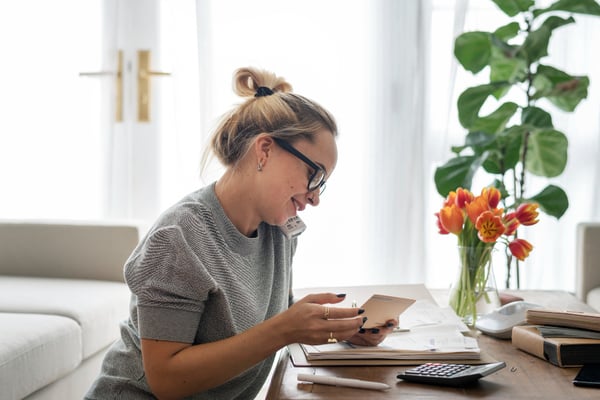 Picture from What is opportunity cost 's article shows a woman sitting on the floor, at a coffee table, on the phone while looking at a piece of paper and with a calculator on the table.