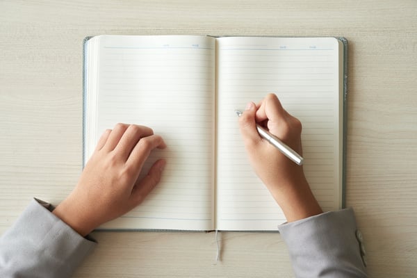 A person holding a pen with an open notebook on a blank page